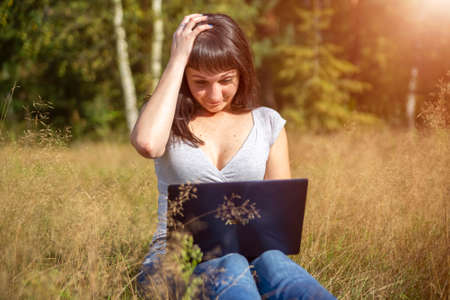 young adult woman looks at a laptop in a panic and holds her head. network problem. shock contentの写真素材