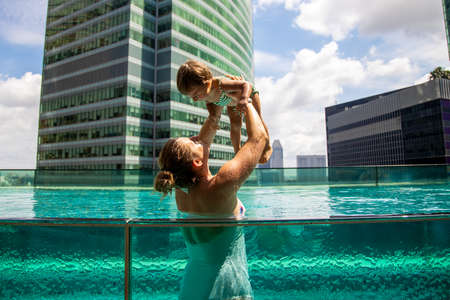 young mother playing with little daughter in the pool on the roof in megapolis city ....