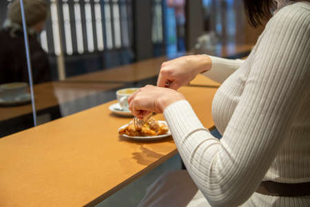 woman cuts croissant and drinks coffee at a table in a cafe. no faceの写真素材