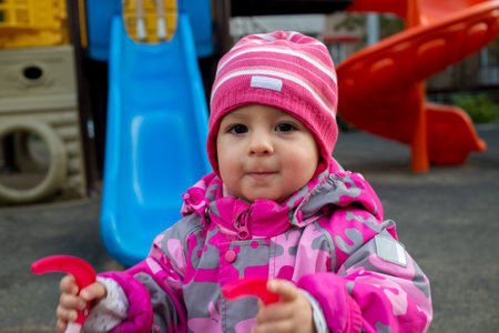 little toddler in warm winter overalls plays on the playground. soft focusの写真素材