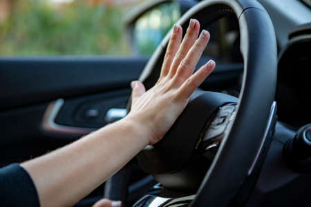 female hand presses the horn on the steering wheel of a modern car. no face