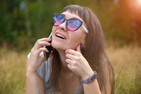 young woman emotionally speaks on the phone on the lawn on a sunny day. happy emotion on the faceの写真素材
