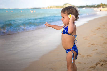 adorable toddler toddler stands on the sandy beach and points at the tropical seaの写真素材