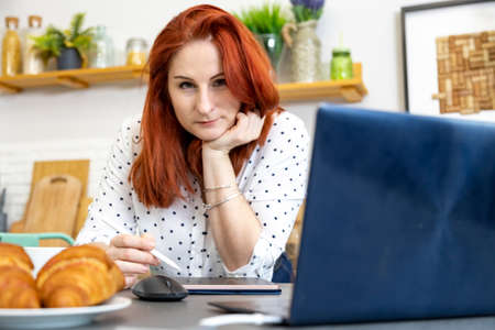 Woman using laptop while sitting at home. Young woman sitting in kitchen and working on laptop. remote workの写真素材
