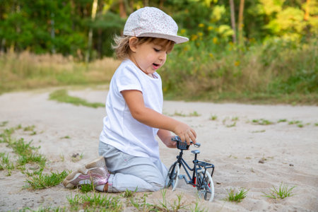 adorable toddler plays with a toy bike in nature. child on all fours in the sand on the lawnの写真素材