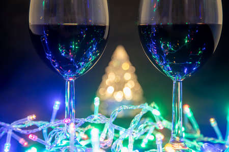 two glasses on the background of a shining Christmas tree and a multi-colored garland on a dark night background. New Year celebration.の写真素材