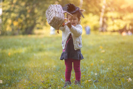 little toddler witch playing with a basket of leaves in autumn park.の写真素材