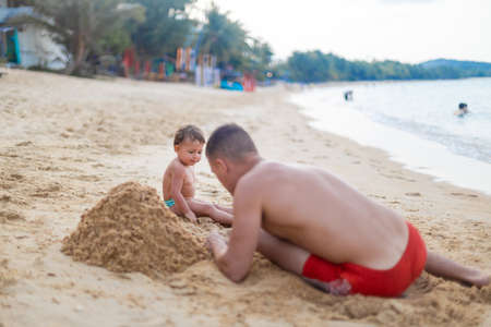 cute toddler kid playing in the sand with father by the sea.の写真素材