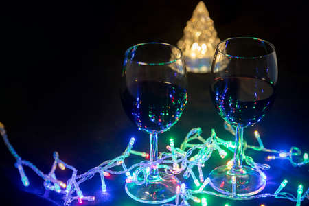 two glasses on the background of a shining Christmas tree and a multi-colored garland on a dark...