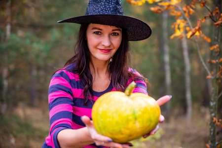 beautiful witch holds out a pumpkin to the camera in the autumn forest