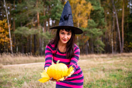 attractive witch with pumpkin in the autumn forest. halloween party concept