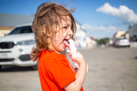 Young Girl Lickling Vanilla Ice Cream outdoors summer day. ice cream melts and flows on handの写真素材