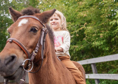 little girl riding pony without saddle on meadow in summer sunny afternoonの写真素材