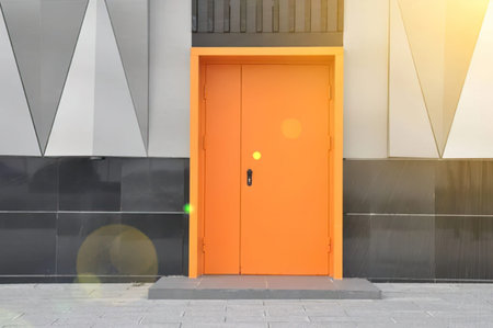 A bright orange door set in a modern building with geometric wall art.