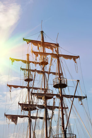 A tall sailing ship with large masts and sails against a clear blue sky.