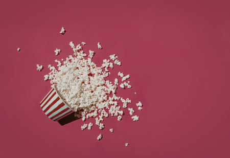 Fresh white popcorn spilling from a striped cup on a bright pink background.