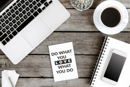 A desk setup with a laptop, notebook, coffee cup, and a motivational quote note.