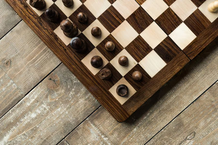 A chessboard with black and white pieces set up on a wooden table