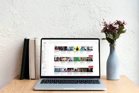 A laptop on a wooden desk with books and a vase of flowers in a cozy home office setup.