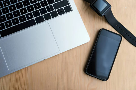A modern workspace with a laptop, smartwatch, and smartphone on a wooden surface.
