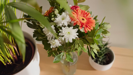 Beautiful flowers arranged in a glass vase on a wooden surface with green leaves