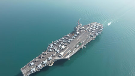 Aerial view of a big aircraft carrier ship moving through calm blue waters.