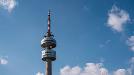 A tall television tower with antennas stands against a blue sky with clouds.
