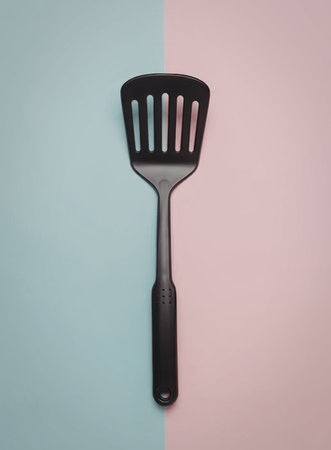 A black kitchen spatula placed on a two-tone pink and blue background.