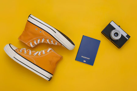 Simple scene with orange sneakers, camera, and passport on bright yellow background