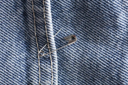 Detailed view of a fabric with a vertical seam and woven pattern, featuring a safety pin