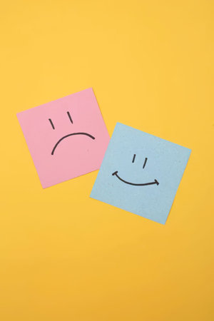 Two sticky notes showing sad and happy faces on bright yellow background