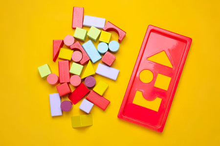 Kids' wooden blocks in bright colors with a red shape sorter toy on yellow surface