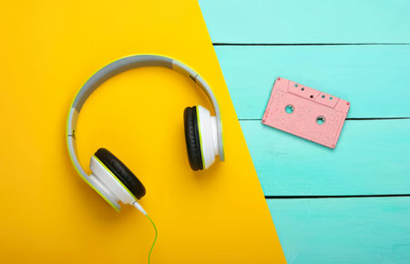 A pair of white and black headphones and pink cassette tape on bright yellow and blue background.