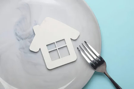 A house shaped paper cutout placed on a plate with a fork, minimalistic scene