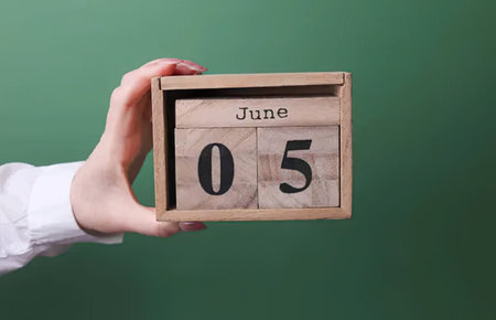 Female hand holding wooden calendar with June 5 date on chalkboard background