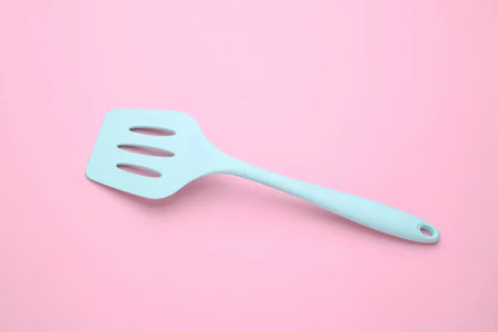 A simple light blue spatula lying on a pink surface, perfect for kitchen use.