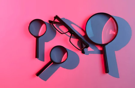 A collection of magnifying glasses and eyeglasses on pink background.