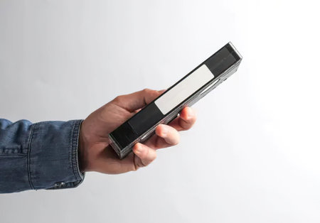 A person in a denim jacket holding a remote control device against a plain white background