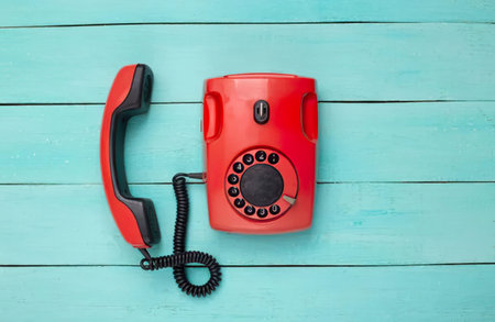 A classic red rotary phone placed on a bright blue wooden background.