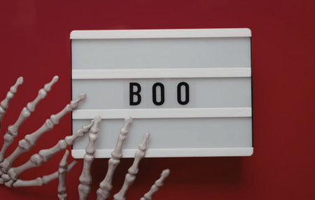 Spooky skeleton hand reaching for a lightbox with the word boo on a red background