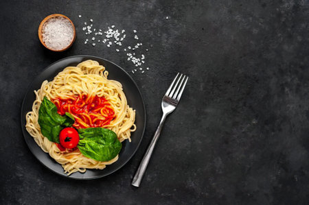 Spaghetti with tomato sauce, basil and spices on black stone background. Top view with copy space