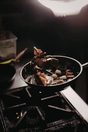 Frying pan with chopped meat and vegetables on a gas stove.
