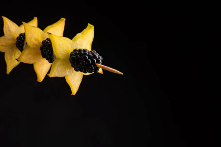 Carambola with blackberries on a black background. Copy space.