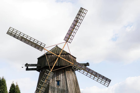 A traditional wooden windmill with four blades stands against a cloudy sky, capturing rural charm.