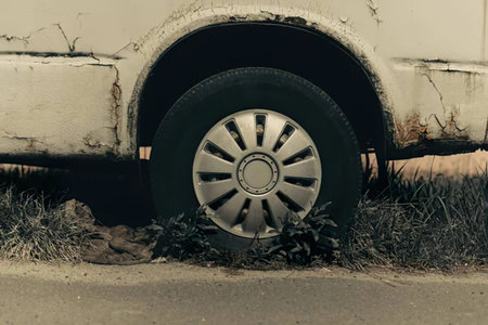 Close-up of a worn-out car tire with cracked vehicle body and grass