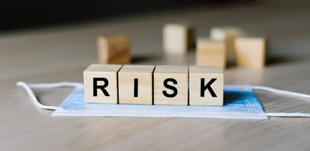Wooden blocks spelling RISK placed on a face mask, with blurred background.