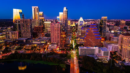 A vibrant cityscape showing tall buildings illuminated at night under a dark blue sky.