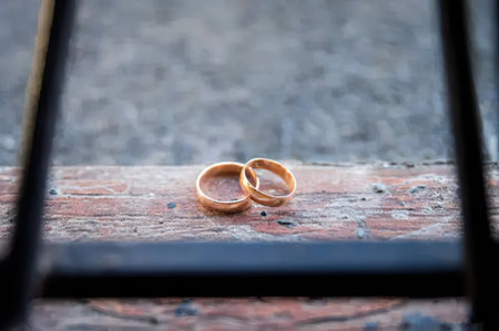 Close-up of two gold wedding rings resting on a brick ledge with black bars in the foreground.