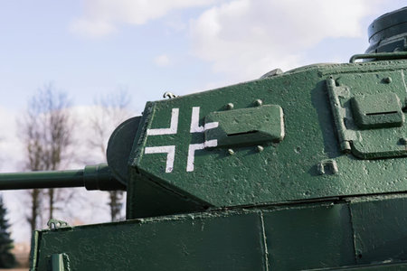 A large green military tank with camouflage paint in an outdoor scene with trees and cloudy sky.