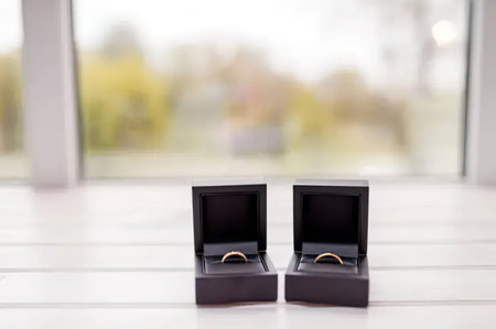 A simple photo of two wedding rings in black jewelry boxes on a white surface with a blurred background.